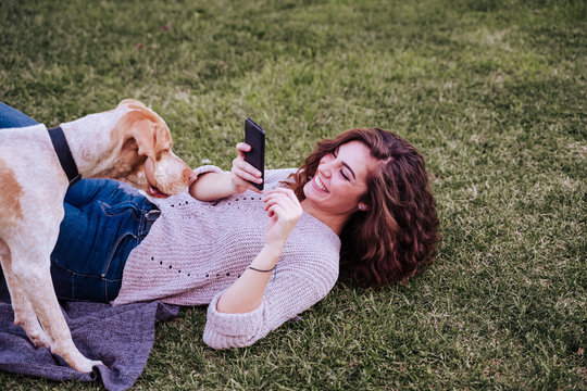 young woman taking a selfie with mobile phone with her dog at the park. autumn season