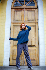Obraz na płótnie Canvas Beautiful red-haired girl in a blue sweater and hat walks through the city