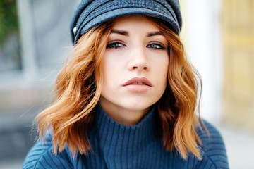 Portrait of a beautiful red-haired girl in a blue sweater and hat. Close up