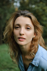 Naklejka premium Blonde girl wearing blue casual jeans blouse is looking at the camera in the park on green trees background