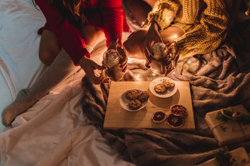 Two friends with a sweater and knee high socks drinking hot chocolate and eating cookies at Christmas by the fireplace.