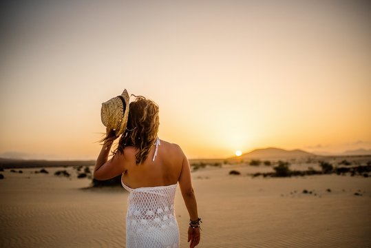 Woman throwing hat into distance to sun