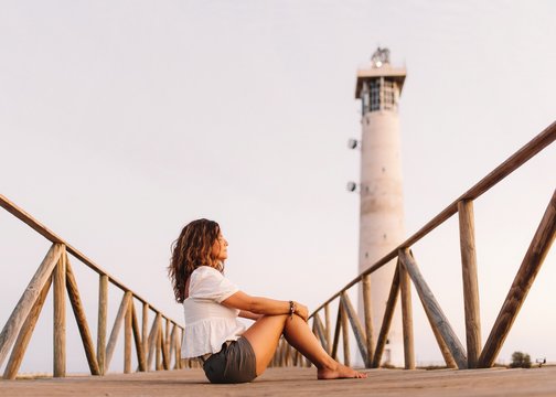 Woman sitting on bridge to lighthouse and looking away
