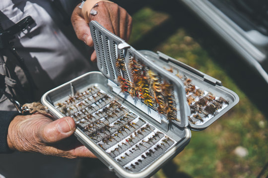 Crop aged man showing arranged lures and hooks while standing on rural street