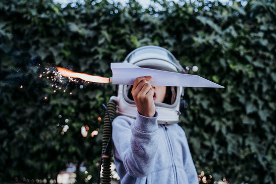 Excited boy in astronaut helmet playing with paper plane with petard in garden
