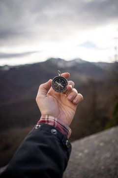 Crop man in jacket holding modern compass in outstretched hand while standing at rocky area