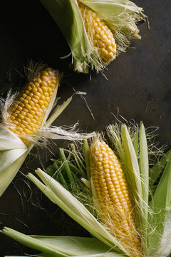 Top view of steps of fresh ripe corn peeling on black table