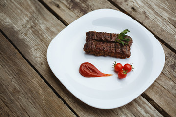 Food in the restaurant. Grilled pork with cherry tomatoes. White plate on a wooden bottom.