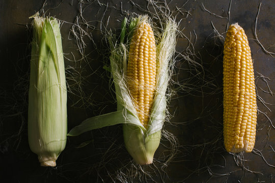 Top view of steps of fresh ripe corn peeling on black table