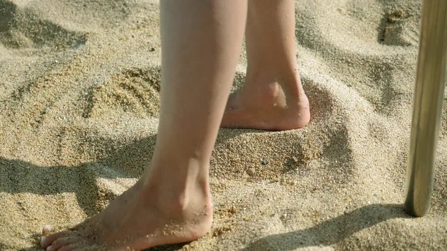Close-up of female feet of a woman standing barefoot on the sand. Slow motion. HD