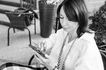 Happy woman in a street cafe reading a text message from her phone. Female making on-line shopping with internet on mobile phone application.  Back and white image