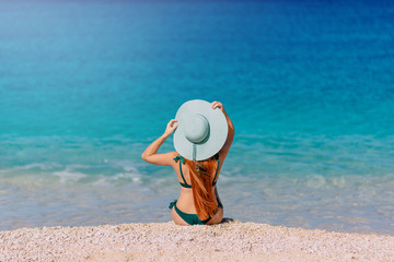 Young woman sits on beach with her back to camera.