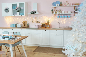Interior of modern white kitchen and decoration on a Christmas New year eve. Pine tree with wrapped gifts and lights
