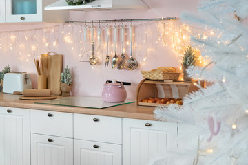 Closeup view on interior of modern white kitchen with pink walls and blue decor on a Christmas New year eve. Pine tree with lights