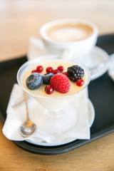 Panna cotta with fresh berries and cap of coffee on the table in  cafe