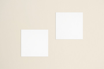 wo empty square white business cards template on bone coloured background. Flat lay, top view....