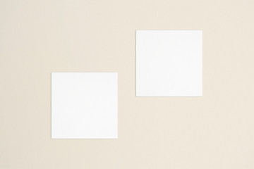 wo empty square white business cards template on bone coloured background. Flat lay, top view. Uneven, open composition. For branding identity, logo design pitches and marketing.
