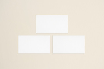 Three empty standard sized white business cards template on bone coloured background. Flat lay, top view. Uneven, open composition. For branding identity, logo design pitches and marketing.