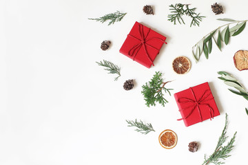 Christmas festive composition, pattern. Olive, cypress tree branches, pine cones, red gift boxes, dry apple, orange fruit on white background. Winter design and decoration. Flat lay, top view.