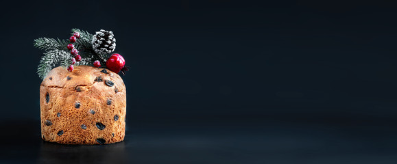 Christmas cake with dried fruits  decorated with fir tree branch, over  black background. Panettone Xmas pastry