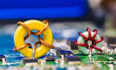 Two colored toroidal induction coils on green circuit board detail. Round magnetic core inductors...