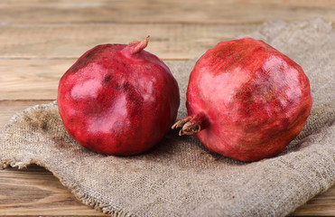 Two ripe pomegranates on burlap on top of a wooden table.