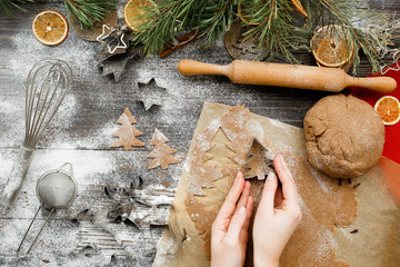 Female hands carve Christmas cookies figures in a christmas tree shape on a kitchen wooden table, ...
