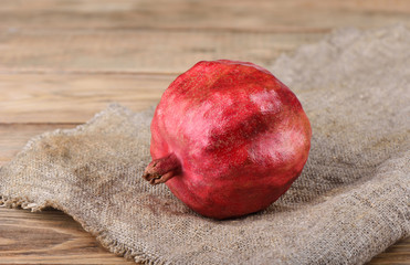 Ripe pomegranate on burlap on top of a wooden table.