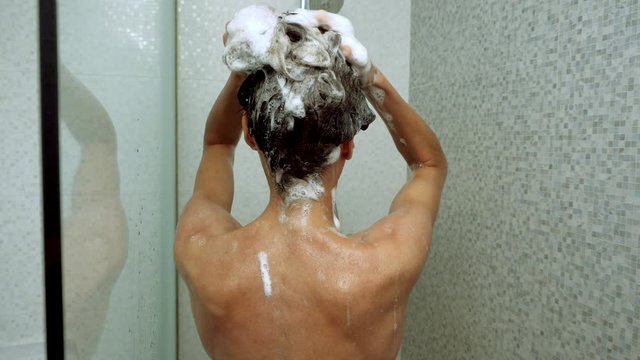 Brunette slim woman washing her hair with shampoo in the shower. Close-up shot from back. Slow motion. HD