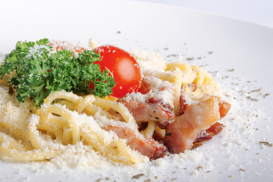 typical spaghetti alla carbonara  with raw egg and bacon. served on a white plate with grated Pecorino cheese. decorated with cherry tomato and parsley. side view close up