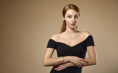 Beautiful girl wearing black off shoulders dress and pearls golden bracelet on beige background