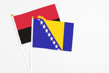 Bosnia Herzegovina and Angola stick flags on white background. High quality fabric, miniature national flag. Peaceful global concept.White floor for copy space.