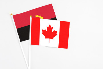 Canada and Angola stick flags on white background. High quality fabric, miniature national flag. Peaceful global concept.White floor for copy space.