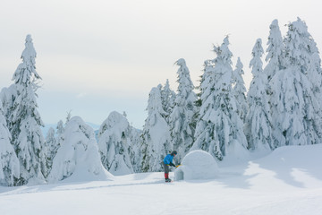 Man in blue jacket building igloo in the high mountain. Fantastic winter scene