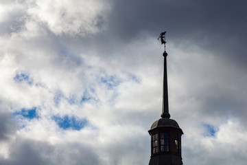 Obraz premium A metal figure of an angel with a trumpet on the spire of a monastery tower against a dramatic sky