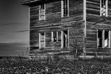 An abandoned house, in black and white, with broken windows and weathered wood siding