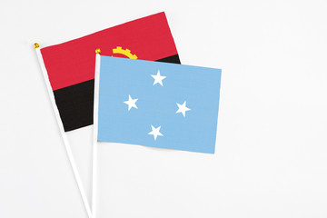 Micronesia and Angola stick flags on white background. High quality fabric, miniature national flag. Peaceful global concept.White floor for copy space.