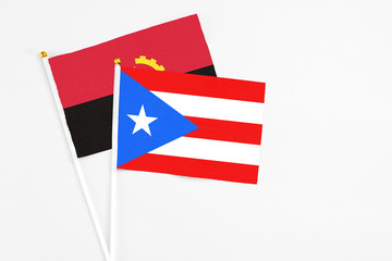 Puerto Rico and Angola stick flags on white background. High quality fabric, miniature national flag. Peaceful global concept.White floor for copy space.