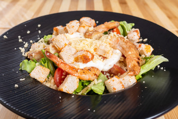 Caesar salad on a black plate, on a wooden background.