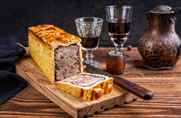Traditional French Pate en croute with goose meat and liver as closeup with red wine on a wooden...