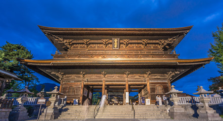Obraz premium Nagano Prefecture, Japan - August 3, 2017: Panoramic view of Motion blurred people walking along Sanmon Gate during blue hour before night at Zenko-ji Temple complex in Nagano city