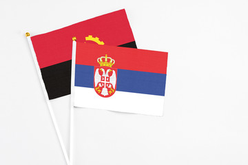 Serbia and Angola stick flags on white background. High quality fabric, miniature national flag. Peaceful global concept.White floor for copy space.