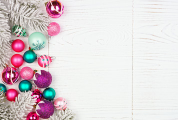 Christmas side border with pink, purple and teal ornaments and tree branches. Above view on a white wood background.