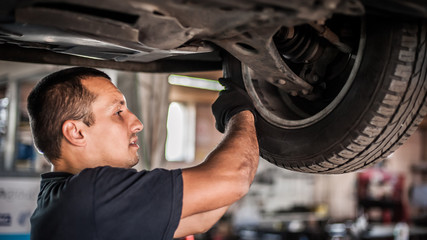 Auto mechanic repairer checking condition under car on vehicle lift
