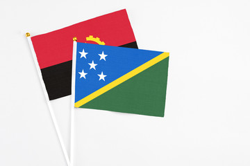 Solomon Islands and Angola stick flags on white background. High quality fabric, miniature national flag. Peaceful global concept.White floor for copy space.