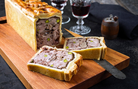 Traditional French Pate en croute with goose meat and liver as closeup with red wine on a modern design wooden board