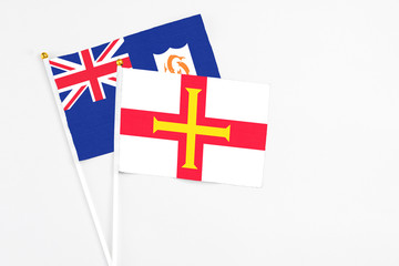 Fototapeta premium Guernsey and Anguilla stick flags on white background. High quality fabric, miniature national flag. Peaceful global concept.White floor for copy space.