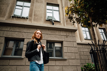 Fototapeta premium beautiful young girl in leather jacket and jeans resting outdoors, portrait of woman in the city