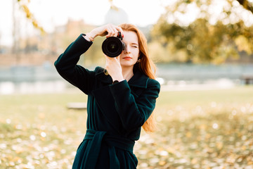 portrait of cute cheerful young girl with amazing red hair posing outdoors holding camera, redhead woman is relaxing on the park