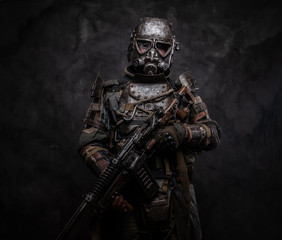 Concept of post - apocalypse futuristic warrior with weapon in hands at dark photo studio.